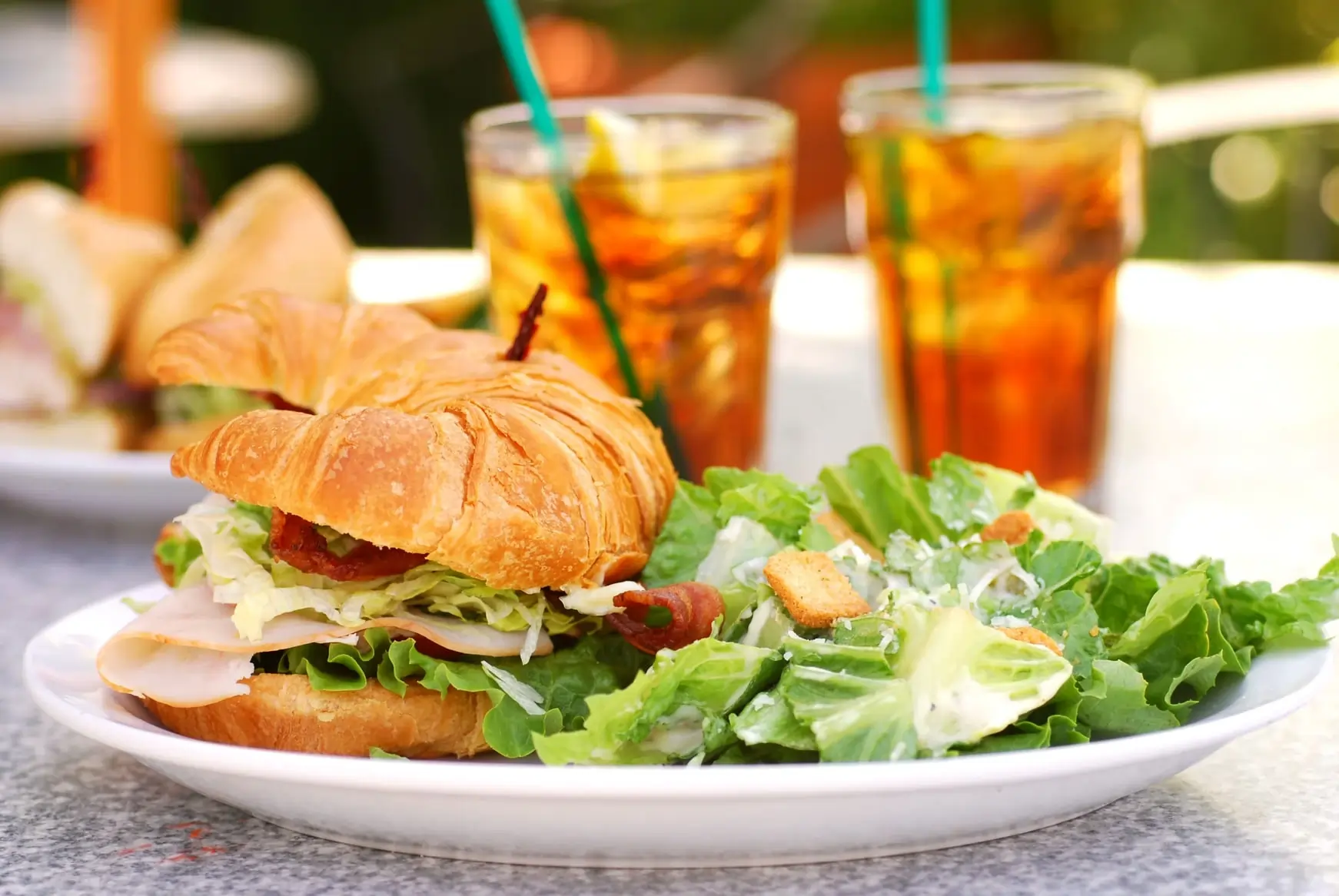 Croissant sandwich with turkey, lettuce, and bacon, served with Caesar salad and iced tea