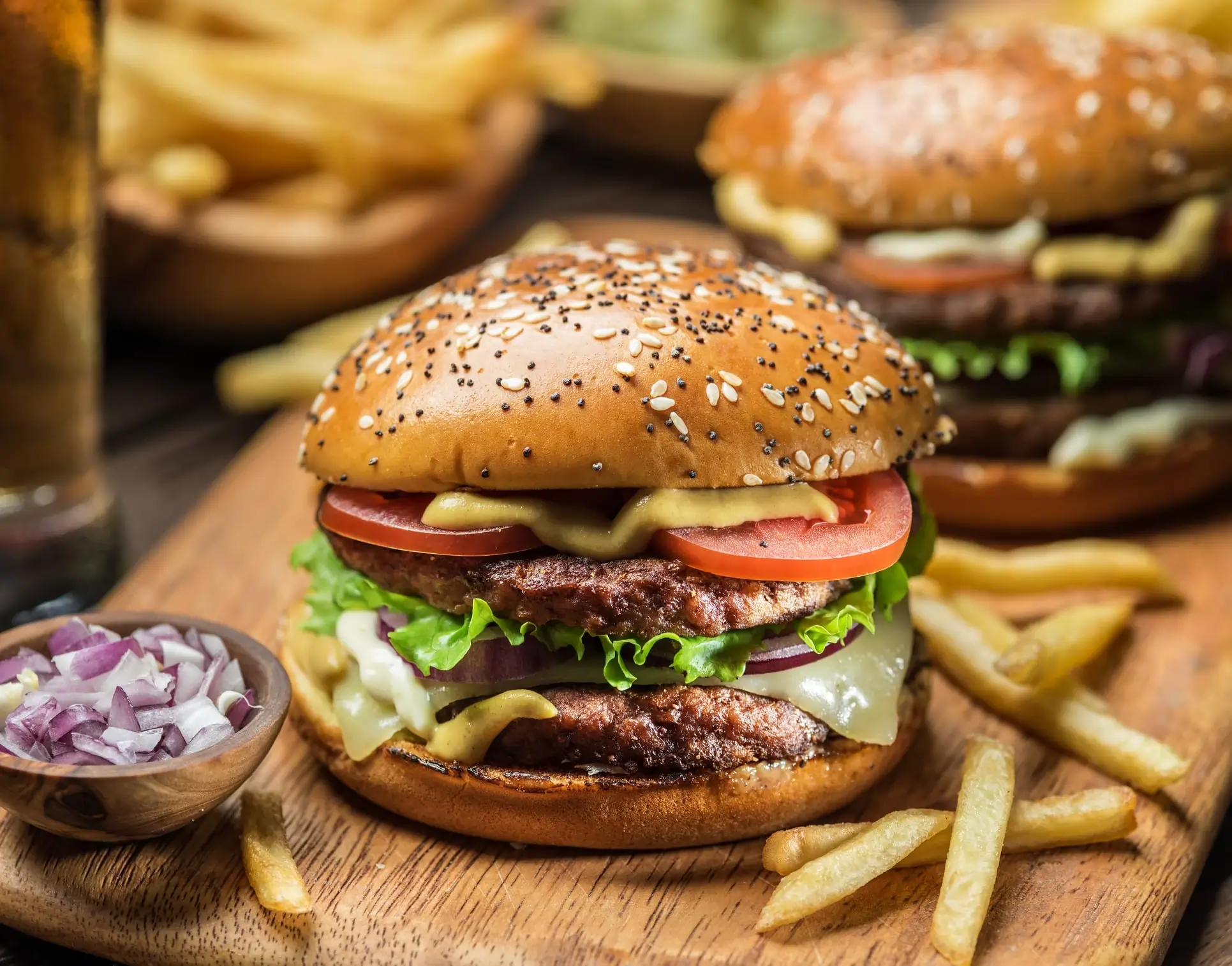 Double cheeseburger with lettuce, tomato, and fries on a wooden board