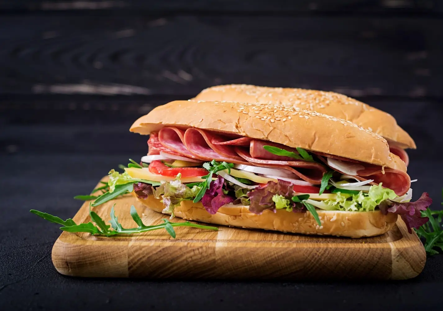 Hoagie sandwich with salami, lettuce, tomato, and cheese on a sesame seed bun